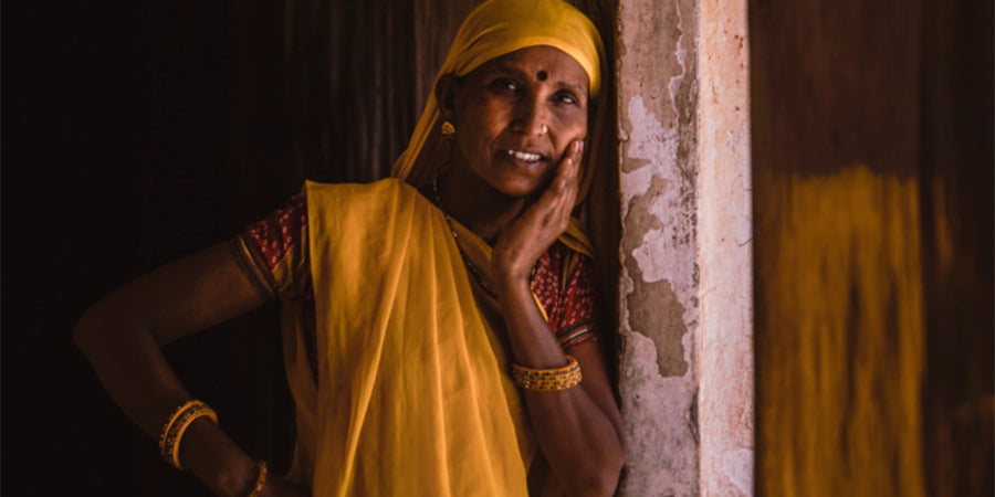 Portrait of a woman in yellow sari leaning against a pillar with her head resting on her left hand